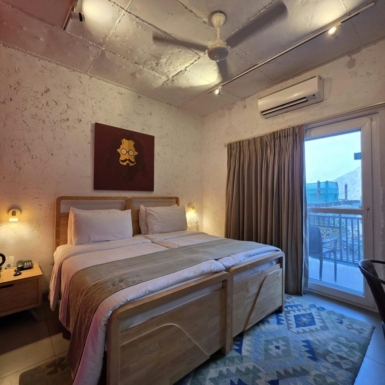 Warm hotel room interior with twin beds and balcony access at sunset.